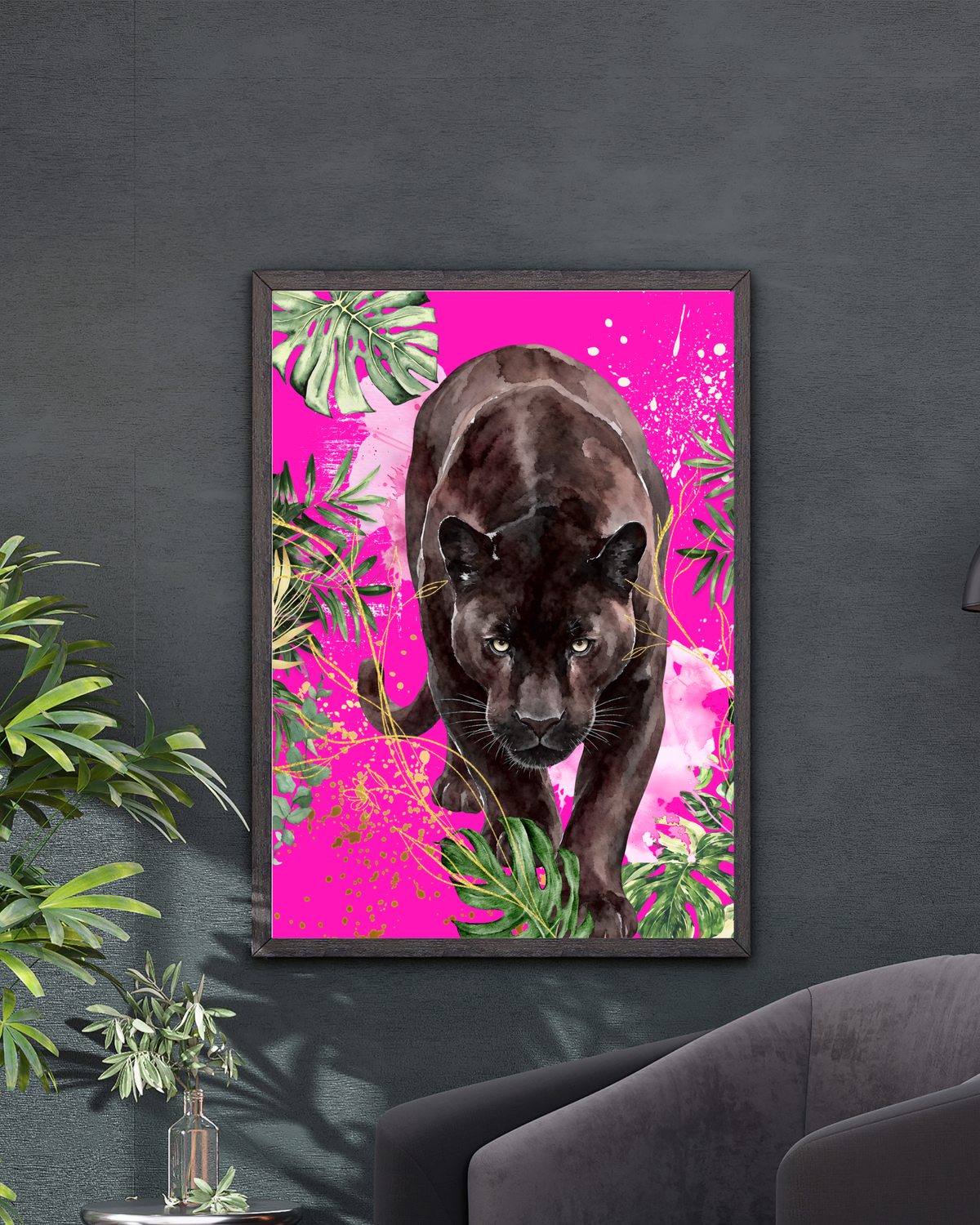 A framed art print featuring a black panther surrounded by bright pink tropical leaves, displayed on a dark gray wall above a modern gray armchair with a small plant nearby.