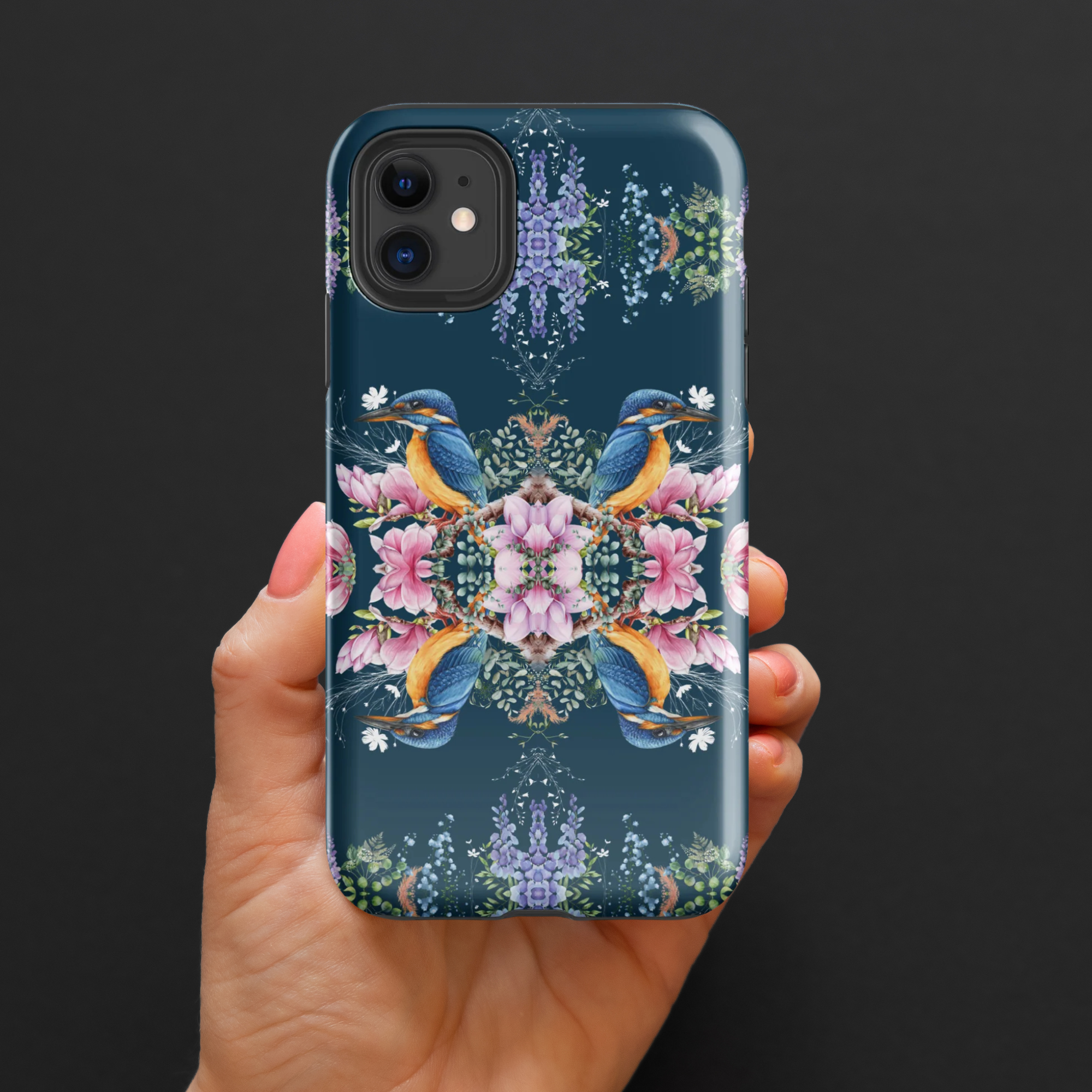 Phone case with floral and bird design held by a hand against a black background